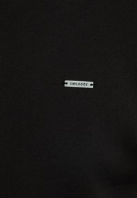 Tela negra con una textura suave que presenta una etiqueta de logo plateado que dice "SMILODOX" colocada en el centro.