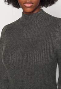 Grå ribbad stickad tröja med hög krage, som har strukturtyg och subtila detaljer på axlarna. Inga synliga mönster eller metalldelar.
