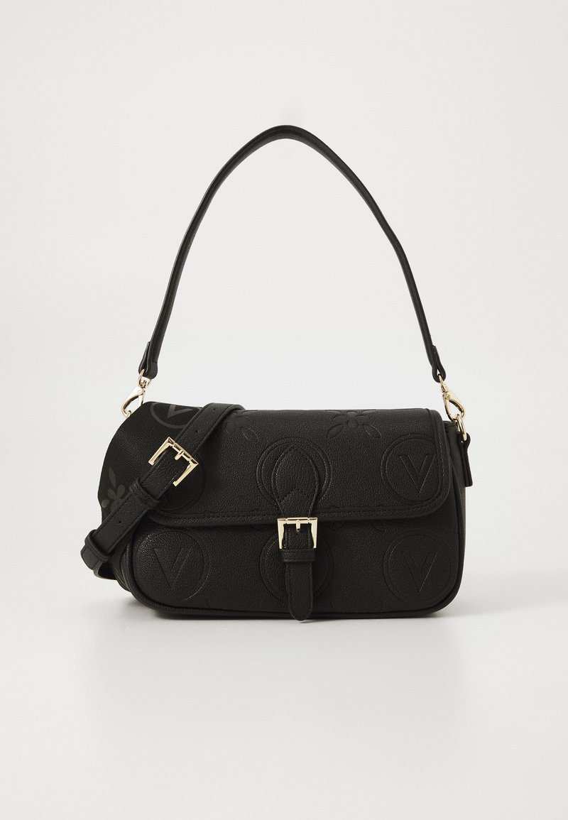 Crna kožna torba preko ramena s reljefnim okruglim uzorcima, zatvaranje s pozlaćenim kopčanjem i podesivim remenom na bijeloj pozadini.