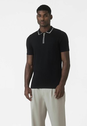 Fekete galléros póló cipzáras nyakkal és fehér csíkozással. Rövid ujjú, testhezálló kialakítás, puha anyag. Világos színű nadrággal párosítva.