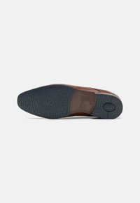 Chaussure en cuir marron avec une tige texturée et une semelle en caoutchouc bleue, présentant des détails complexes et un marquage en relief sur la semelle extérieure.
