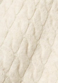 Tissu tricoté de couleur crème avec un motif en torsades, présentant une texture douce et duveteuse. Le design met en valeur des formes en relief entrelacées.
