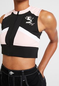 Top atlético recortado en negro y rosa con cremallera frontal, que presenta un detalle de raya blanca y un logo en el lado izquierdo. Fabricado en material elástico.