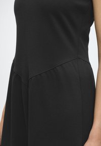 Gros plan d'une robe noire sans manches avec des détails de couture en diagonale à la taille et une jupe évasée.