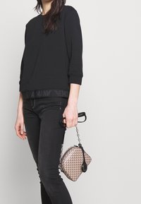 Černá bavlněná mikina s tříčtvrtečními rukávy a strukturovaným pasem, kombinovaná s tmavými úzkými džínami a malou vzorovanou kabelkou.