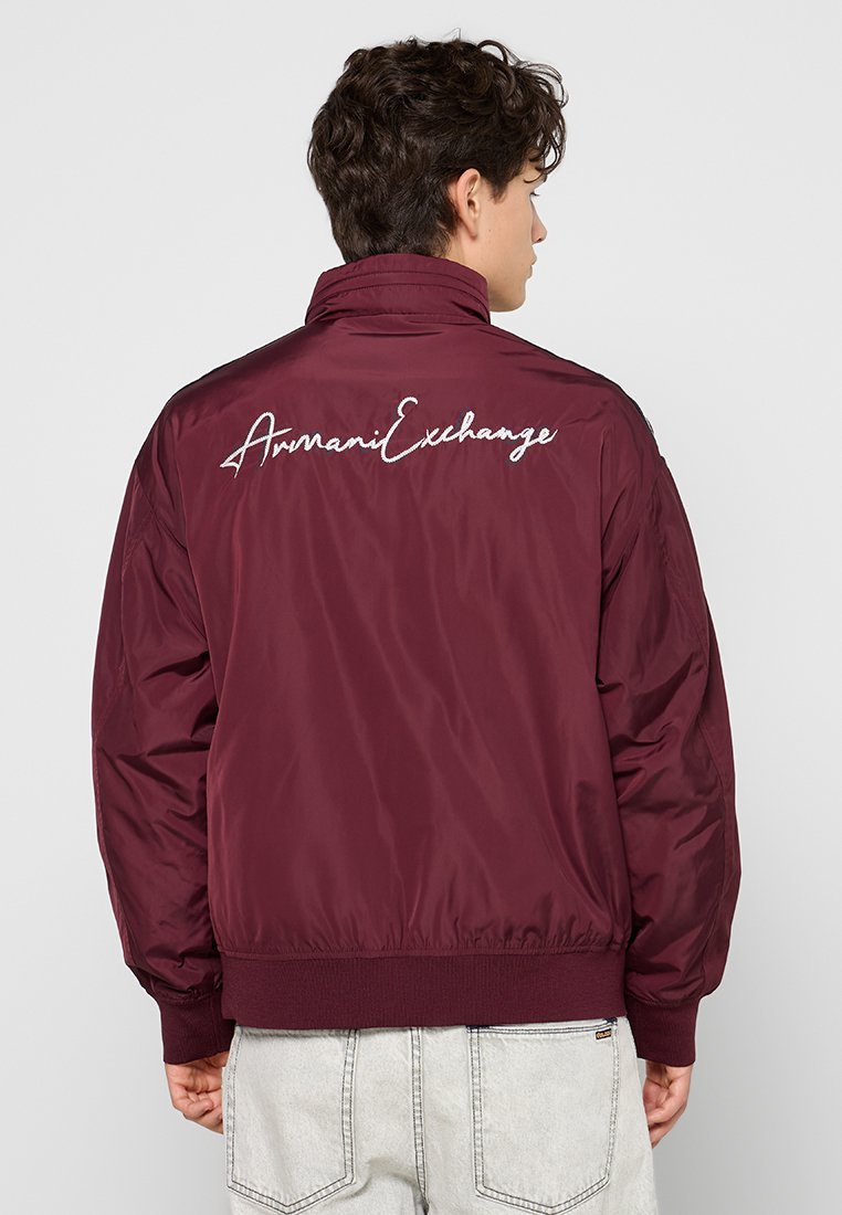 Giacca bomber bordeaux con una texture liscia e lucida, caratterizzata da un logo ricamato bianco sul retro e polsini e orlo a coste.