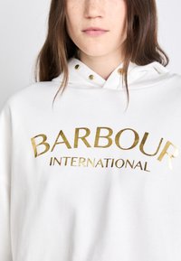 White hoodie with a drawstring hood, featuring a gold printed logo "BARBOUR INTERNATIONAL" across the front in bold lettering.
