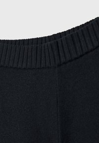 Gros plan d'une ceinture de vêtement noire comportant un élastique côtelé avec un corps en tissu lisse et une couture visible.