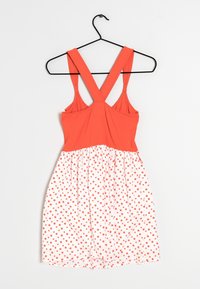 Robe rouge sans manches avec des bretelles croisées. La partie supérieure est unie rouge, et la jupe est en tissu blanc avec des pois rouges.