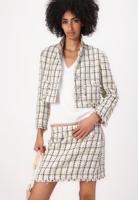 Ensemble de veste et jupe en tweed avec un motif à carreaux multicolore. La veste présente un design court, des fermetures à boutons et des bords effilochés.