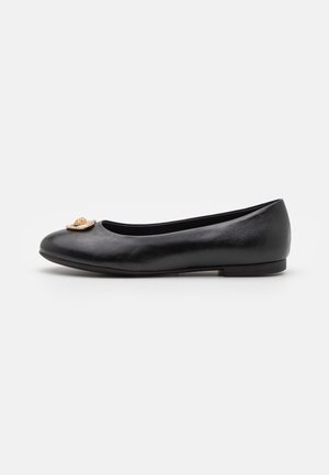 Chaussure plate en cuir noir avec bout rond et emblème décoratif doré à l'avant, vue de côté sur fond blanc.