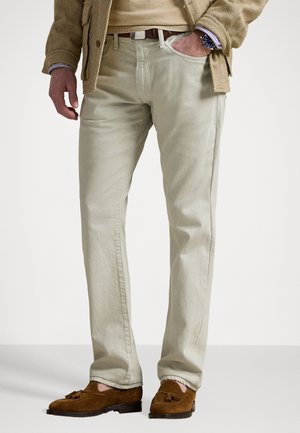 Pantalones de algodón twill beige con corte recto, bolsillos frontales y cinturón de cuero marrón; combinados con mocasines de ante marrón.