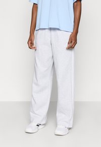 Világosszürke melegítőnadrág puha anyagból, laza szabással, oldalsávokkal és rugalmas derékrésszel. Fehér tornacipővel párosítva.