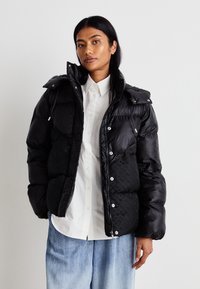 Musta puhvitakki kiiltävällä pinnalla, vetoketjulla edessä, napillisella sulkemisella ja hupulla. Sisältää tikatun kuvion ja sivutaskut.