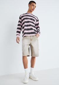 Långärmad randig skjorta i rosa och svart; beige shorts; vita sneakers med ljusa accenter; textil med struktur; avslappnad passform.