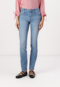 Jeans de denim azul claro con un corte ajustado, cintura alta y un ligero desvanecimiento. Combinados con unos zapatos planos negros de punta redonda y una blusa de rayas rojas.