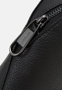 Borsa in pelle nera con texture, dotata di chiusura a zip; presenta una zip in metallo argentato e un'etichetta con il logo Calvin Klein attaccata.