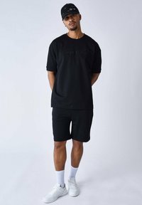 T-shirt noir à manches courtes et shorts assortis, en mélange de coton, coupe décontractée, avec des accents de logo brodés. Baskets blanches, chaussettes côtelées.