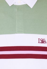 Koszulka polo z jasnoróżową górną częścią, białym środkowym pasem i poziomymi paskami w kolorze czerwonym/różowym. Materiał bawełniany, z kołnierzykiem i zapięciem na guziki.