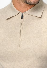 Beige Poloshirt mit Kragen und Halbreißverschluss, aus weichem, strukturiertem Stoff. Verfügt über ein sauberes, minimalistisches Design ohne Muster oder Logos.