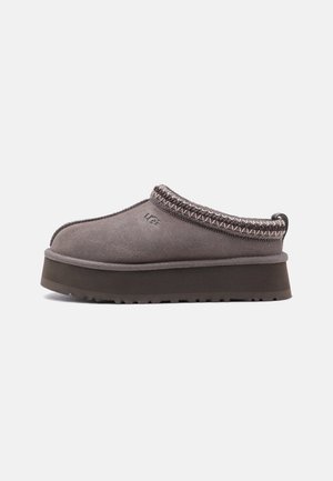 Chaussure à enfiler en daim gris avec semelle épaisse, bordure tressée autour de l’ouverture et logo UGG sur le côté.