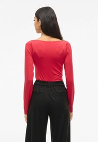 Czerwona bluzka z długim rękawem i okrągłym dekoltem, zestawiona z czarnymi, luźnymi spodniami z elastycznym pasem i kieszeniami bocznymi.