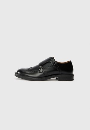 Czarny skórzany elegancki but typu monk strap z detalami brogue i podwójnymi klamrami, pokazany z profilu na jasnym tle.