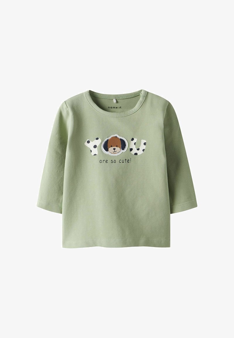 Camisa de manga larga verde claro con un gráfico de perro y el texto "¡ERES tan lindo!". Material de algodón suave con cuello redondo y ajuste holgado.