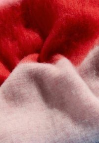 Textúrovaná vlnená tkanina s kombináciou červenej a jemnej ružovej farby. Farby sa hladko spájajú a zdôrazňujú mäkkú, chlpatú textúru.