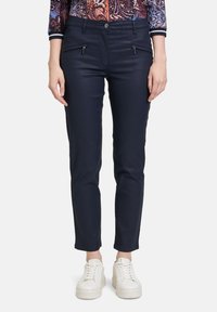 Marineblaue Slim-Fit-Hosen aus elastischem Material, mit Reißverschlusstaschen und glatter Textur, kombiniert mit weißen Plateausneakern.