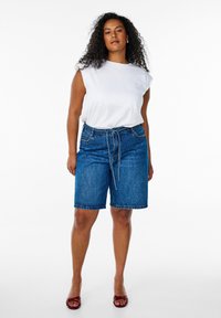 Jeansshorts i mörkblått med avslappnad passform, featuring dragsko i midjan, sidofickor och en slät vit ärmlös topp.