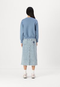 Light blue sweatshirt with ribbed cuffs, paired with a light blue denim skirt featuring back pockets and floral embroidery.