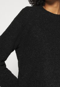 Pull noir texturé avec une finition douce et duveteuse. Présente un col rond et des manches longues, mettant en avant un design confortable et décontracté.