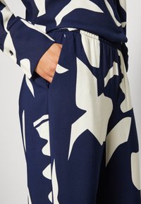 Navy fabric with a large white abstract pattern; shirt with buttoned cuffs, paired with elastic-waist trousers featuring side pockets.