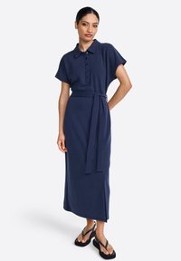 Abito blu navy con maniche corte, chiusura anteriore con bottoni, vita regolabile con cintura e spacco laterale. realizzato in un morbido tessuto testurizzato con una vestibilità rilassata.