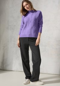 Pull en maille violet avec un motif en chevrons surélevé, col rond, manches à poignets côtelés, associé à un pantalon gris foncé et des baskets blanches sur un fond clair.