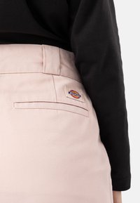 Světle růžové kalhoty s kapsou na zadní straně a malou, vícebarevnou nášivkou Dickies. Hladký, bavlněný materiál s přiléhavým střihem.