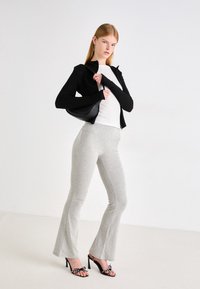 Crna zip-up jakna preko bijele pripijene majice, sivi široki hlače i crne sandale s visokom petom s dekorativnim detaljima. Glatke teksture.