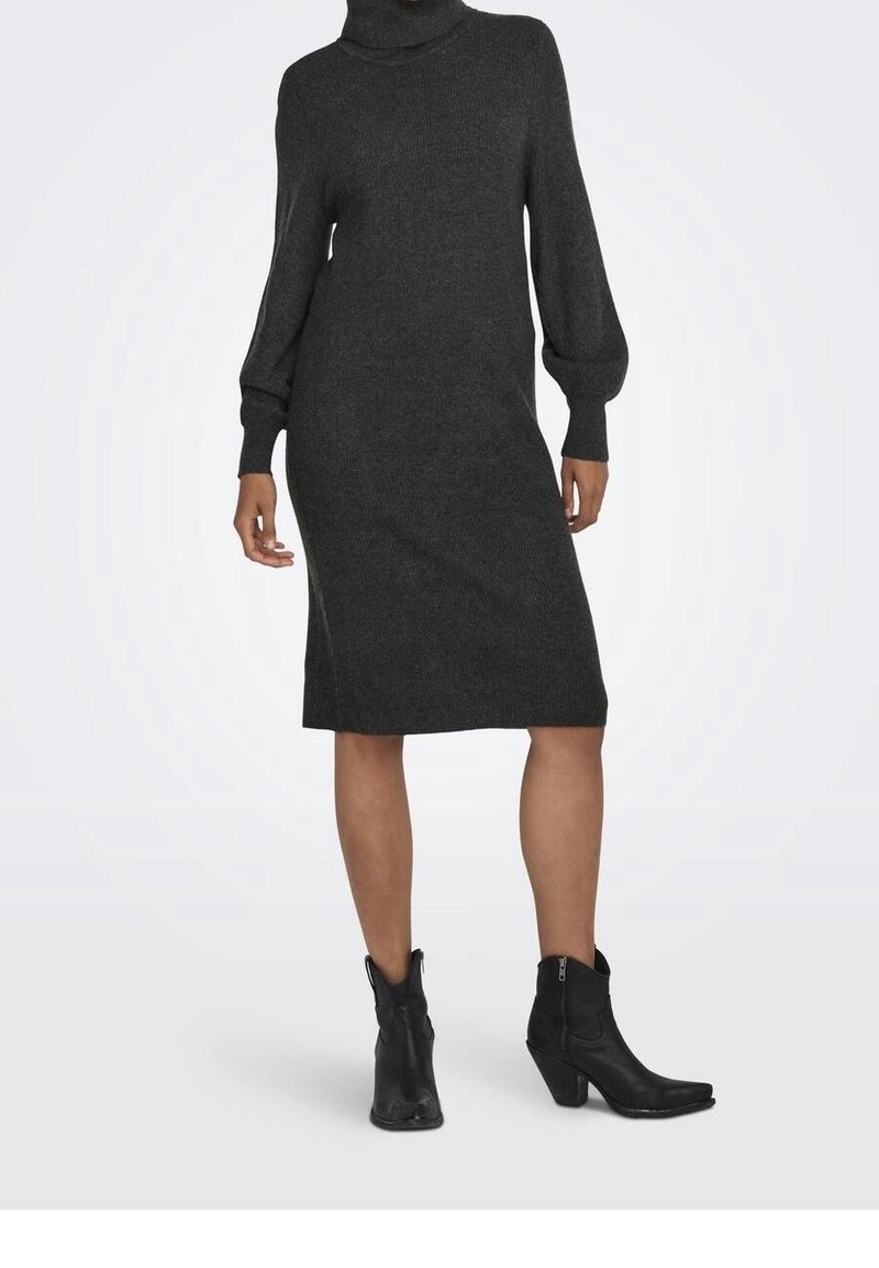 Robe col roulé en maille côtelée grise avec manches longues, atteignant le milieu du mollet. Associée à des bottines noires avec un détail zippé.