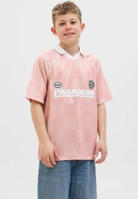 Camiseta de fútbol rosa de manga corta con un patrón a cuadros, detalles en blanco y logo de "PASADENA". Cuello tipo polo. Se lleva con shorts de mezclilla.
