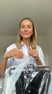 Vêtements noirs sur un cintre recouverts de plastique transparent. Le vêtement a une étiquette attachée et une étiquette blanche avec un logo noir visible.