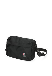 Černá nylonová messenger taška se zipovým uzávěrem, nastavitelným popruhem a předním klopovým víkem. Obsahuje malou nášivku s logem na dolní části přední strany.
