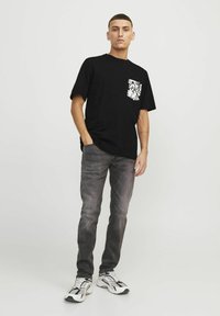 Camiseta negra de manga corta con bolsillo y diseño floral blanco, combinada con jeans grises y zapatillas en blanco y negro.