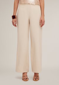 Wijde benen broek van lichtbeige stof, met twee zijzakken, een zachte textuur en een losse pasvorm. Gecombineerd met sandalen met verstelbare banden.