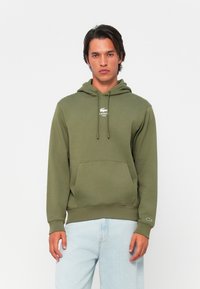 Olijfgroene hoodie van zachte stof, met een kangoeroe-pocket, trekkoord capuchon en een wit Lacoste-logo op de borst.