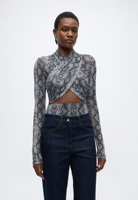 Haut à manches longues imprimé peau de serpent en gris et noir, avec un design cache-cœur et un détail découpé. Associé à un jean taille haute bleu foncé.