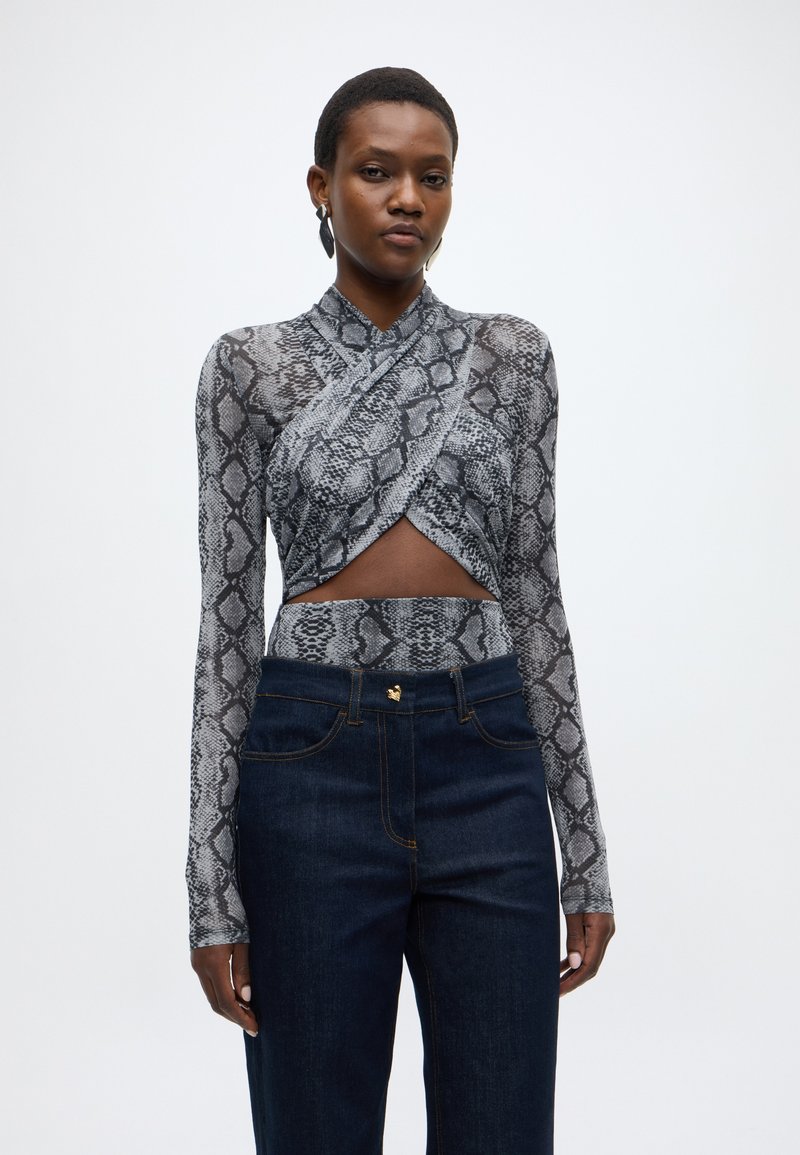 Haut à manches longues imprimé peau de serpent en gris et noir, avec un design cache-cœur et un détail découpé. Associé à un jean taille haute bleu foncé.