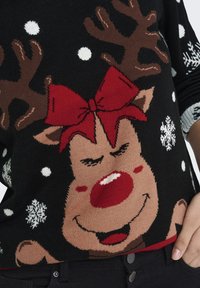 Maglione nero lavorato a maglia con un design di renna con corna marroni, un fiocco rosso e fiocchi di neve bianchi. La texture è morbida e decorata.
