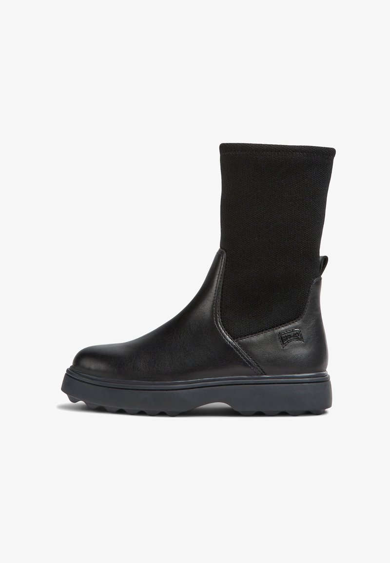 Bottines noires avec un corps en cuir lisse et une tige en tissu noir texturé. Semelle en caoutchouc épaisse avec un motif de traction et un onglet latéral.