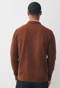 Brauner Strickpullover mit strukturierter Oberfläche, ausgestattet mit einem gerippten Kragen und Bündchen. Das Design weist eine gerade geschnittene Silhouette auf.